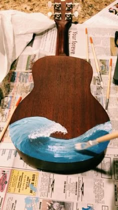 a wooden guitar sitting on top of a table covered in paper and paintbrushes