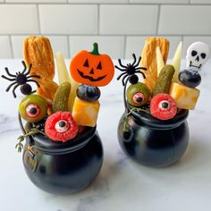 two black pots filled with halloween treats on top of a table