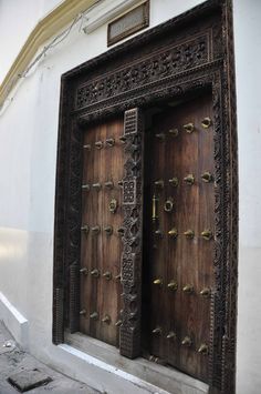 two wooden doors with ornate carvings on the side of a white building in an alleyway