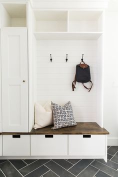 a white coat rack with two coats hanging on it's sides and a black purse sitting on the top shelf