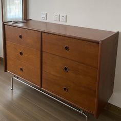 a wooden dresser sitting on top of a hard wood floor next to a wall mounted light switch