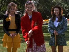 three women standing in the grass with one holding a stick