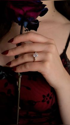 a woman with red nails holding a flower in her hand and wearing a diamond ring