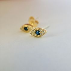 These Sapphire Evil eye earrings are simple yet elegant. Comfortable so much that you forget you have them on! Evil eye earring, Tiny gold studs, Blue Cz delicate earrings are made with 925 Sterling Silver and plated with 18 carat gold with cz natural Sapphire blue Zirconium stones.  Evil eye is an ancient image of protection, used throughout history in different cultures. When a person wears an evil eye with them, it guards against misfortune happening in one's life. Increase your earring colle Gold Evil Eye Earrings As Gift, Yellow Gold Evil Eye Earrings For Gift, Gold Round Evil Eye Earrings, Gold Plated Evil Eye Elegant Earrings, Elegant Evil Eye Earrings As A Gift, Elegant Evil Eye Earrings For Gift, Elegant Gold Plated Evil Eye Earrings, Elegant Gold-plated Evil Eye Earrings, Diamond Eyes Drop Earrings As Gift