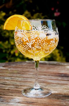 a glass filled with yellow liquid sitting on top of a wooden table next to flowers