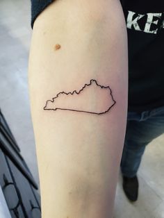 a small outline tattoo on the arm of a woman's left leg, with mountains in