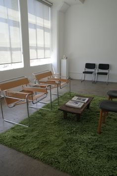 an empty waiting room with four chairs and a green rug on the floor in front of two windows