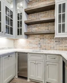 a kitchen with gray cabinets and white marble counter tops, built into the side of a brick wall