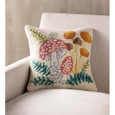 a white chair with a mushroom pillow on it's back and an embroidered cushion in the middle