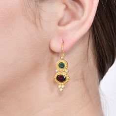 a close up of a woman's ear wearing gold earrings with garnets and pearls