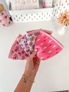 a hand holding three small pink and white flowered hair clips on top of a table