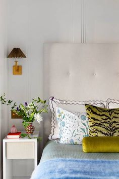 a bed with blue and green pillows on top of it next to a white night stand