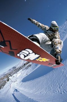 a snowboarder is doing a trick in the air on his red and white board