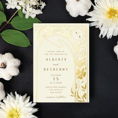 the wedding card is surrounded by white flowers and greenery on a black background with gold foil