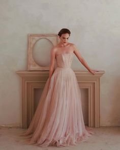 a woman in a pink dress standing next to a fireplace