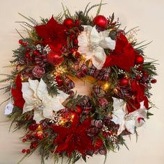 a christmas wreath with red and white poinsettis, greenery and lights