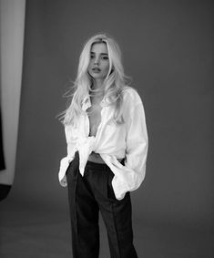 a woman standing in front of a white wall wearing black pants and a white shirt