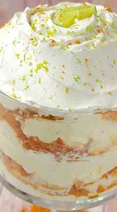 a layered cake with white frosting and limes on top is sitting in a glass dish