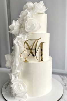 a three tiered white wedding cake with flowers on the side and monogrammed initials