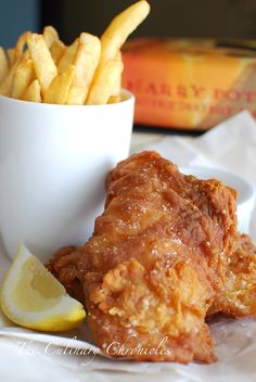 fried chicken and french fries are served in a white bowl with lemon wedges on the side