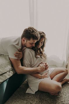 a man and woman cuddle on the floor in front of a window while holding each other