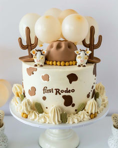 a cake decorated with white frosting and brown fondant, topped with balloons in the shape of animals