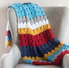 a crocheted blanket sitting on top of a gray chair next to a white wall