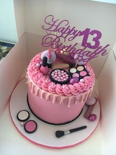 a birthday cake with pink icing and makeup on top, in a white box