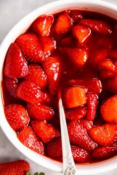 a bowl filled with sliced strawberries next to a spoon