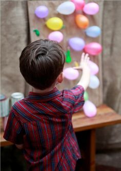 a young boy standing in front of a wooden table with balloons on the wall behind him