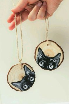 two black cats painted on wood slices hanging from string with hand holding it up to the camera