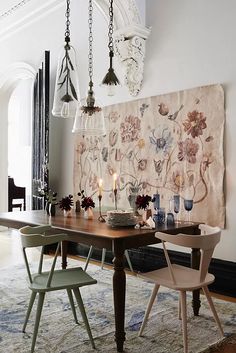 a dining room table with two chairs and a tapestry hanging on the wall