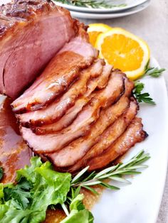 a white plate topped with sliced ham and greens next to an orange wedged in bread