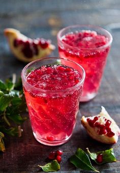 two glasses filled with red liquid sitting on top of a wooden table next to leaves