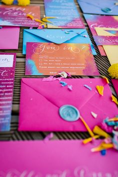 bright pink and blue wedding stationery with yellow pom poms on the table