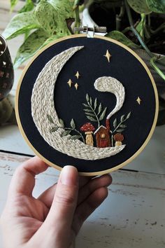 someone is holding up a hand embroidered hoop with a house on the moon in it