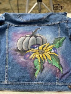 a jean jacket with an image of a sunflower painted on the back of it