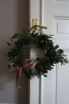 a wreath hanging on the front door of a house with gold ribbon and green leaves