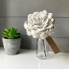 a flower made out of newspaper sitting on top of a table next to a potted plant