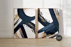 two framed art pieces with black and gold paint strokes on them in an empty room