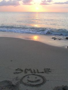 a smiley face drawn in the sand on a beach with waves coming in and sunset behind it