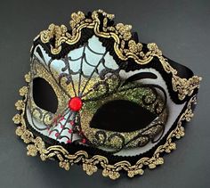 a masquerade mask with gold and black decorations on the side, against a gray background