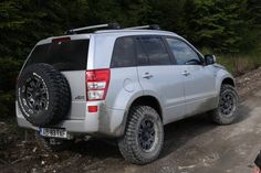 a silver suv parked on the side of a dirt road next to some green trees