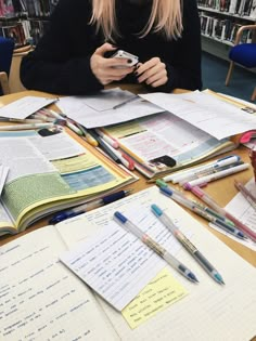 a woman sitting at a table in front of books and writing on her cell phone