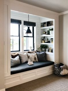 a window seat in the corner of a room with bookshelves and potted plants