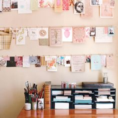 a wooden desk topped with lots of papers and pencils next to a wall covered in pictures