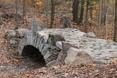 an old stone bridge in the woods with lots of leaves on the ground around it