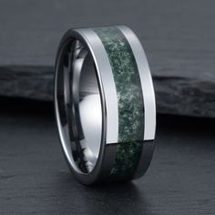 a wedding band with green moss inlays and white ceramic inside, on a black surface