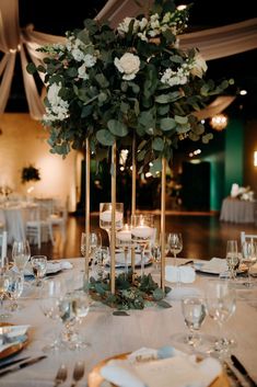 a tall centerpiece with white flowers and greenery sits on top of a table