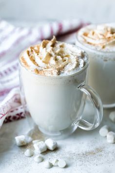 two mugs filled with hot chocolate and marshmallows on a white surface